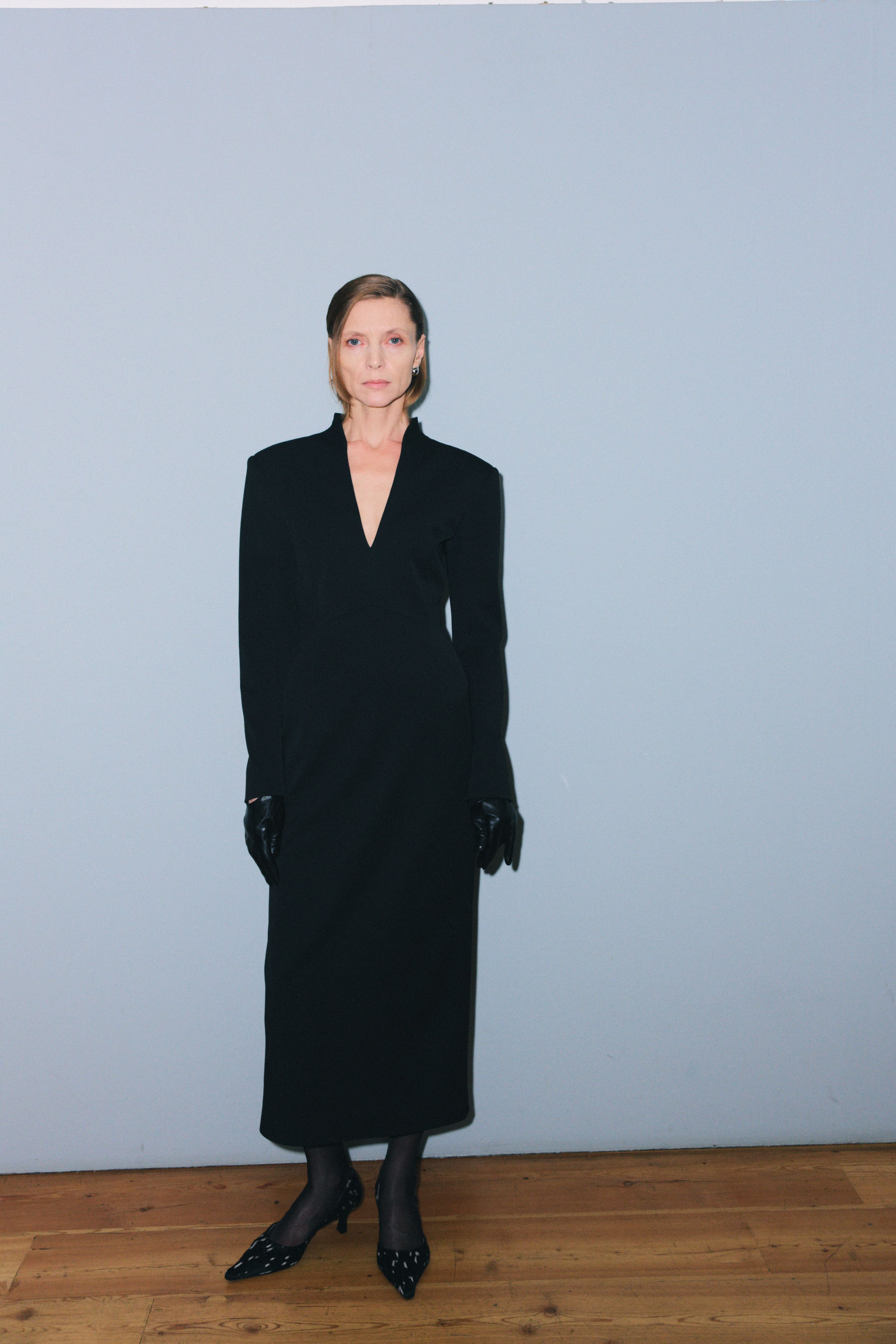 Элегантное черное платье с глубоким вырезом и длинными рукавами, дополненное кожаными перчатками и туфлями с узором.