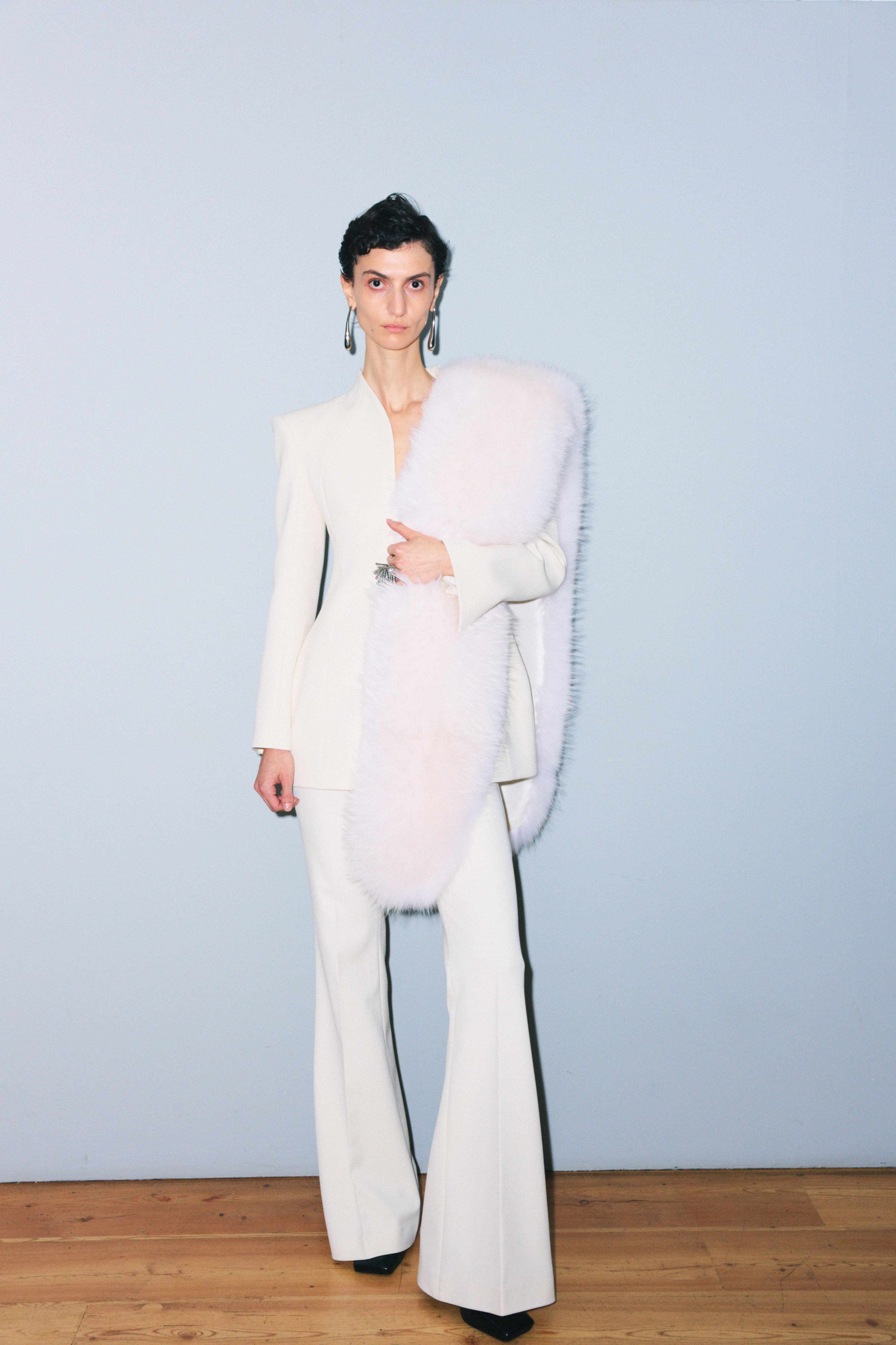 Элегантный белый костюм с расклешенными брюками и глубоким вырезом, дополненный пушистым палантином нежного розового оттенка.