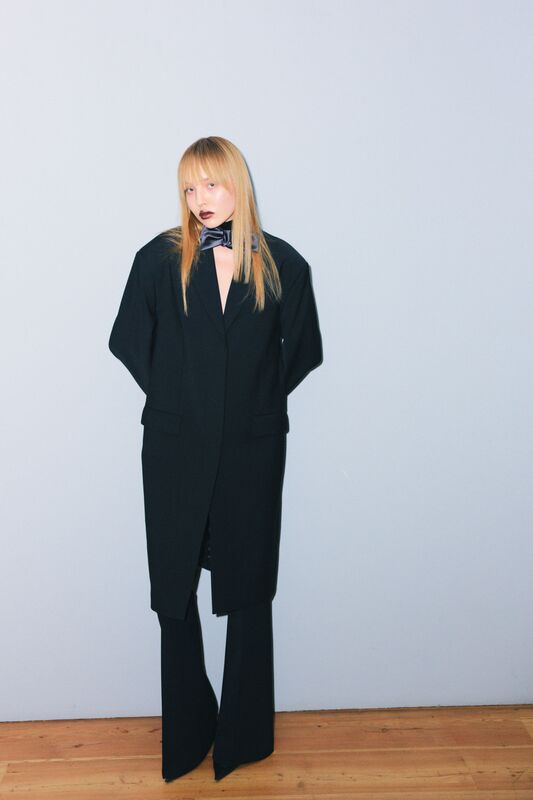 Элегантный черный костюм с глубоким вырезом и широкими брюками, дополненный стильным галстуком, создает атмосферу уверенности и современности....