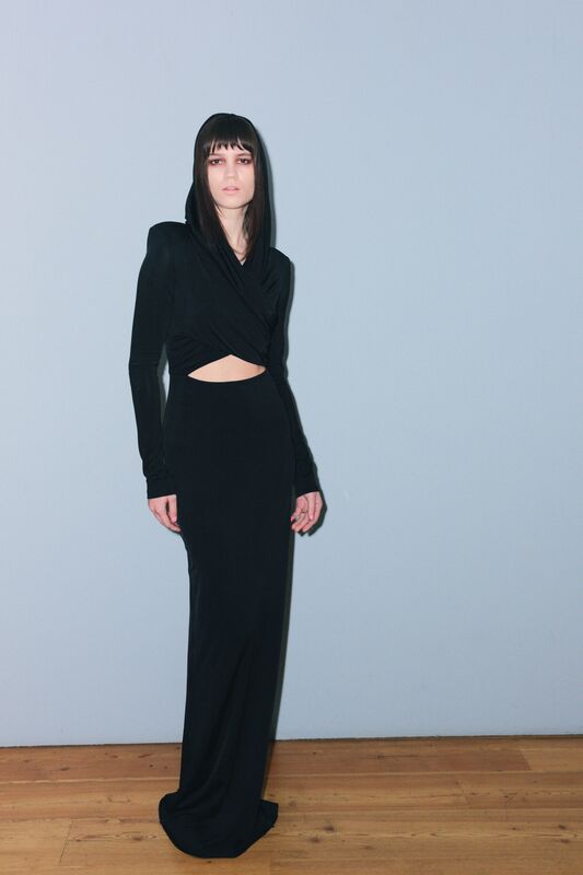 Элегантное черное платье с капюшоном и вырезом на талии, подчеркивающее силуэт, создает атмосферу загадочности и стиля.