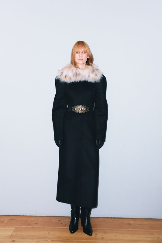 Элегантное черное пальто с меховым воротником и золотым поясом, создающее контраст с гладкими кожаными перчатками и ботфортами.