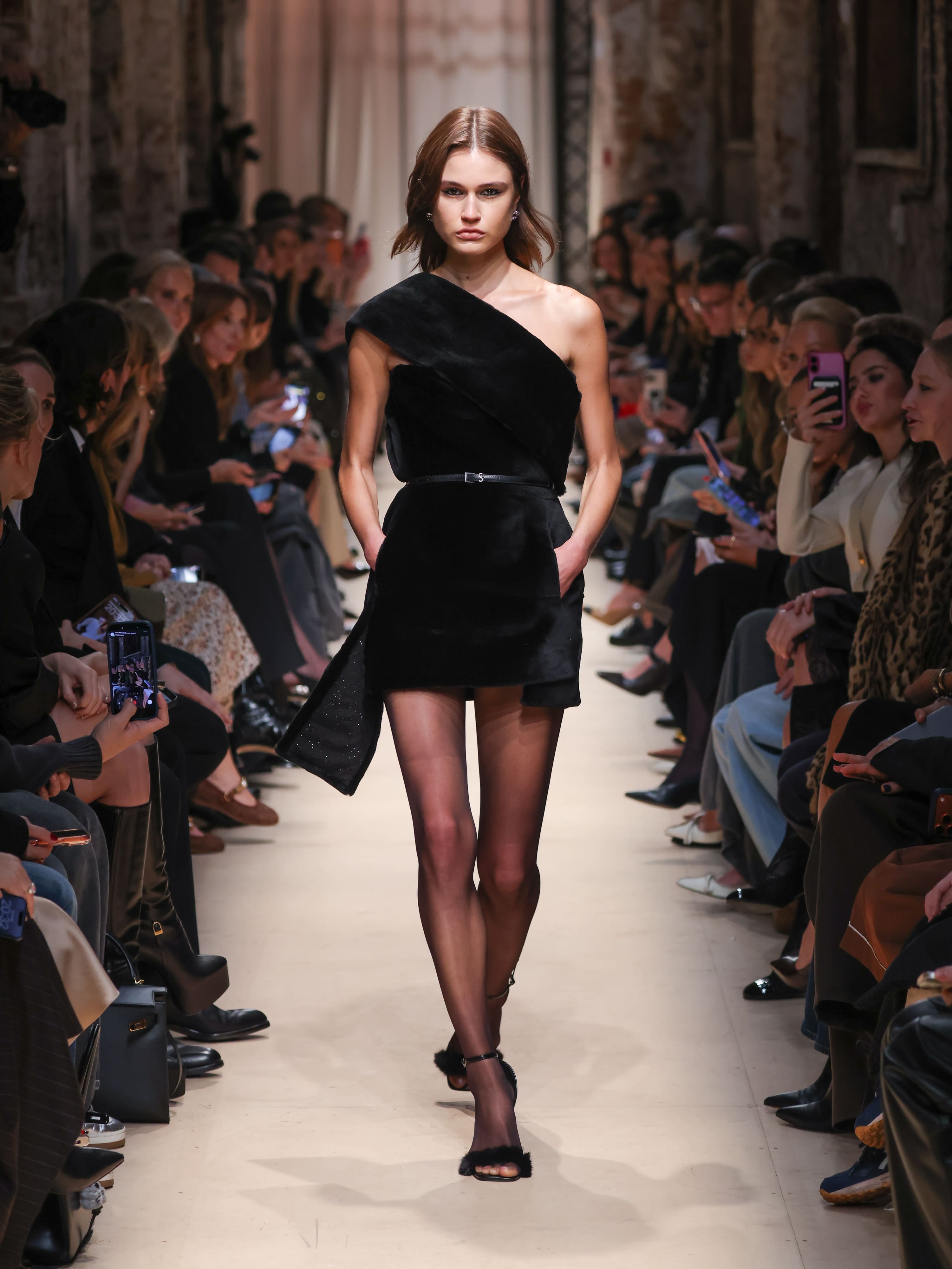 Элегантное черное мини-платье с асимметричным вырезом, подчеркнутое тонким поясом, создает эффектный образ для осени-зимы 2026.