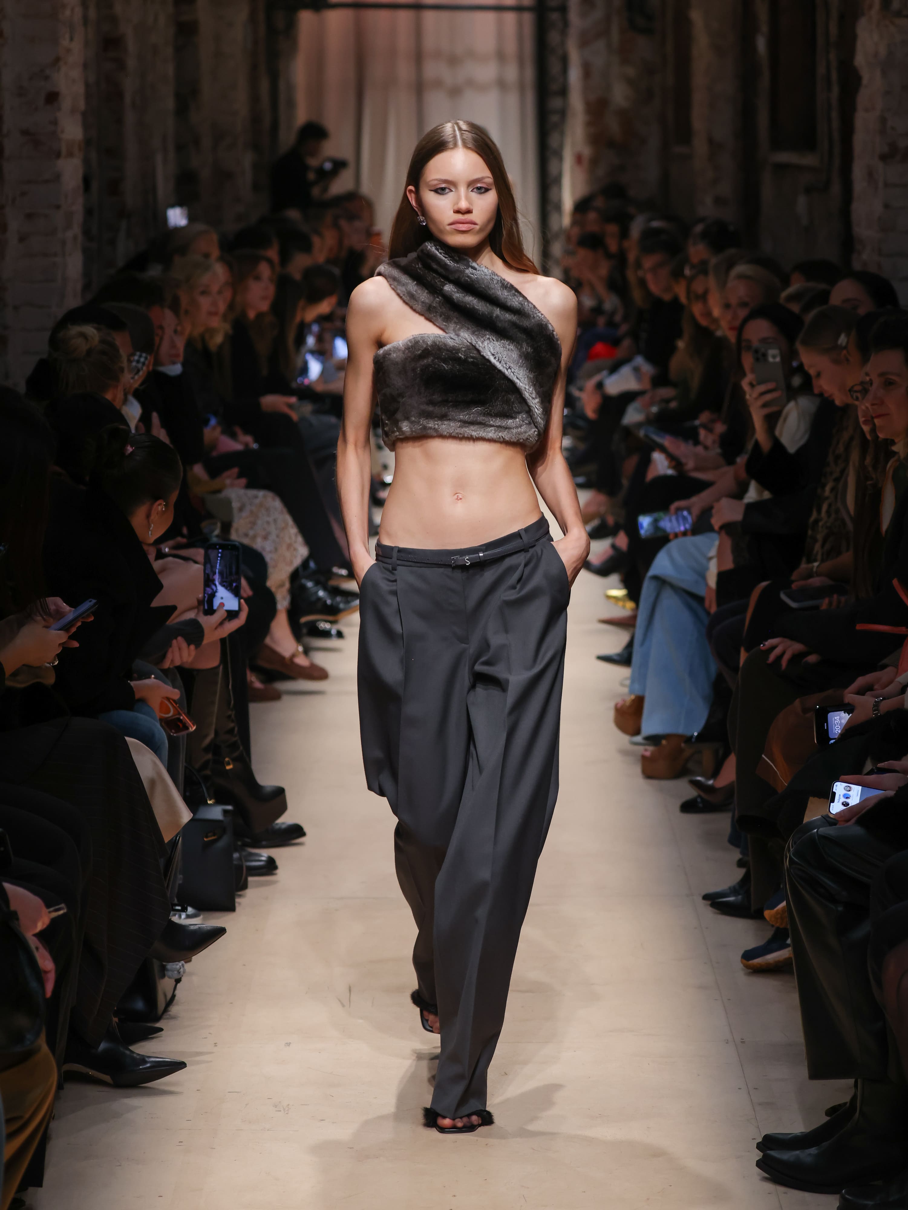 Модель в асимметричном меховом топе и широких брюках серого цвета, создающих контраст с её стройной фигурой, на показе Sashaverse осень-зима 2026.