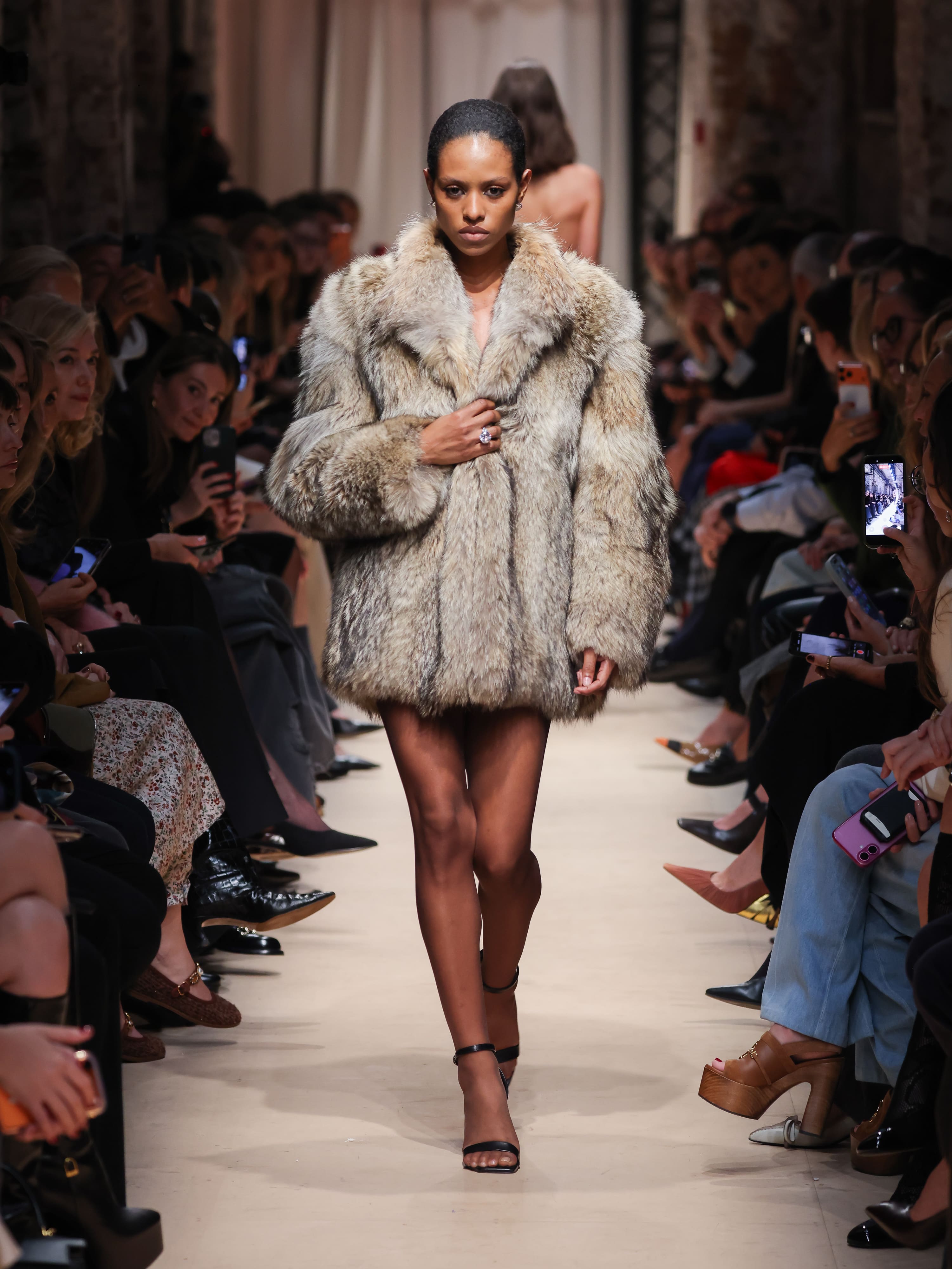 Модель в объемном меховом пальто цвета серого песка, сочетая роскошь и минимализм, уверенно шагает по подиуму Sashaverse осень-зима 2026.