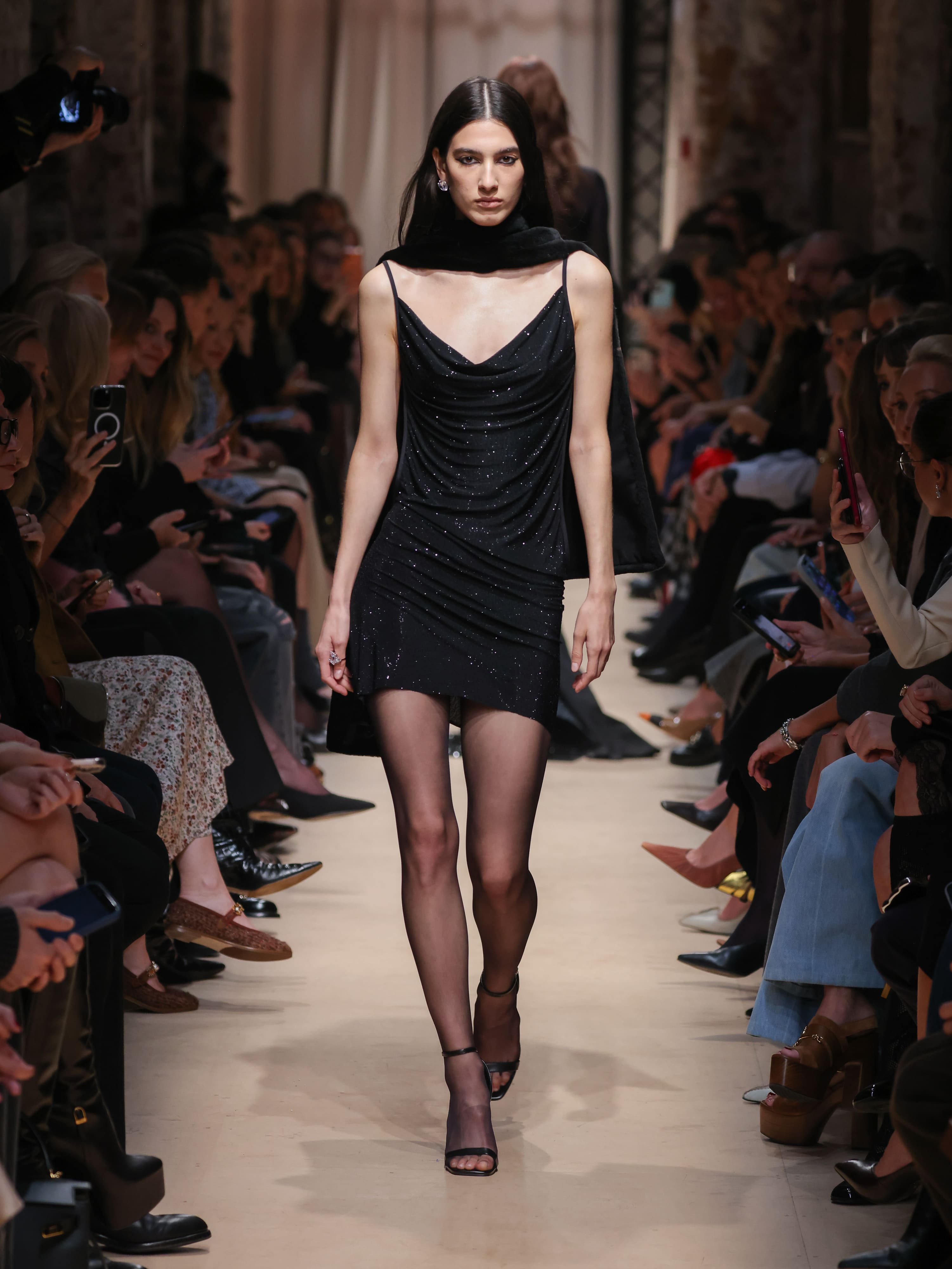 Элегантное черное мини-платье с драпировкой и блестками, дополненное черным шарфом, создает атмосферу вечернего шика.