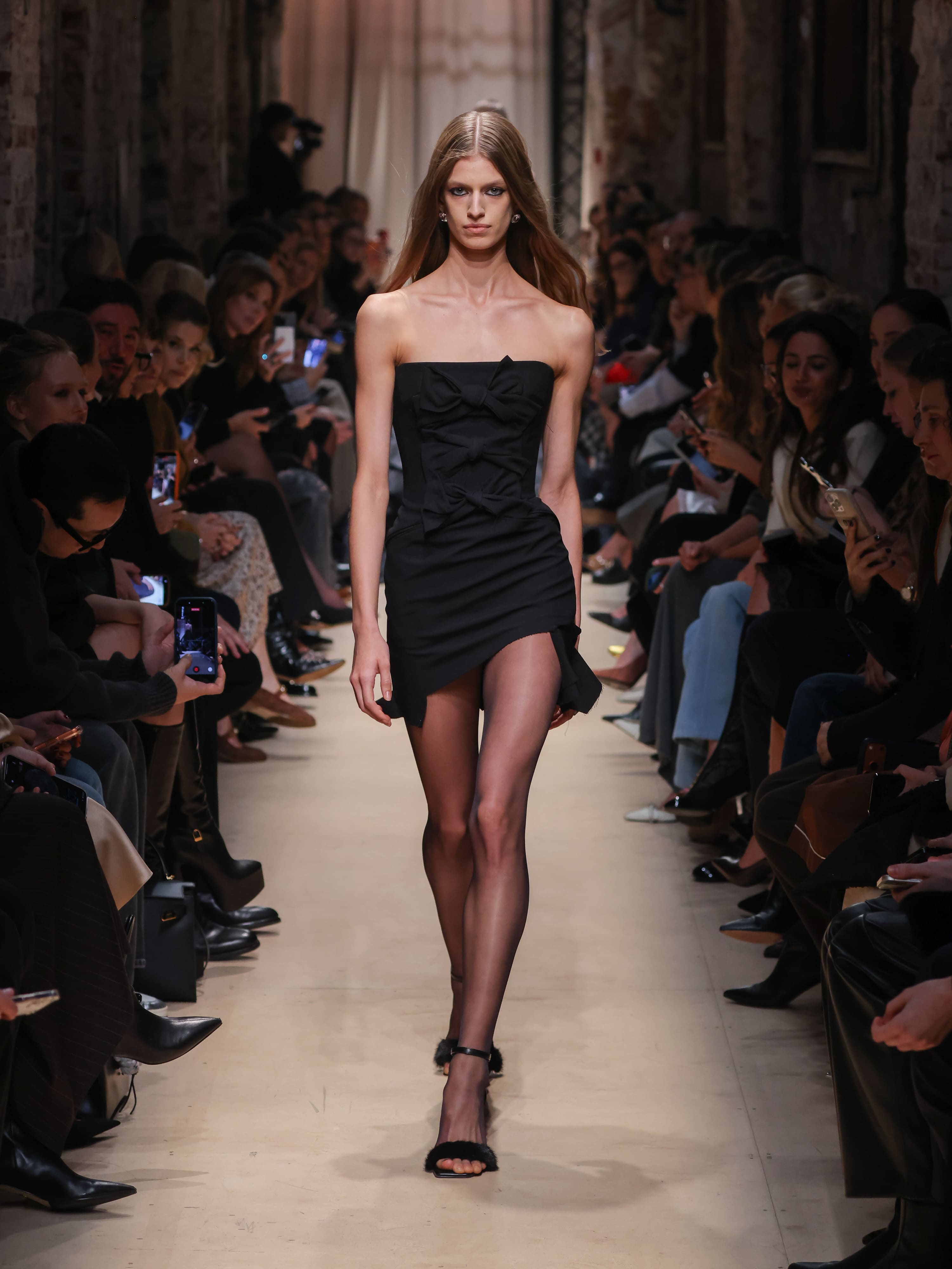 Элегантное черное мини-платье с объемным бантом, подчеркнутое прозрачными колготками, создает эффектный образ для осени-зимы 2026 от Sashaverse.