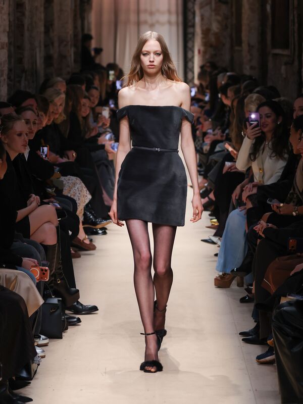 Модель в черном мини-платье с открытыми плечами и тонким поясом, эффектно сочетает элегантность и современность на показе Sashaverse осень-зима 2026....