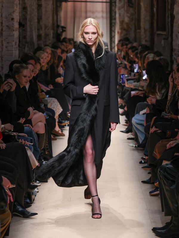 Элегантное черное пальто с длинным меховым шарфом, подчеркивающее стройную фигуру модели, создает атмосферу утонченной роскоши.