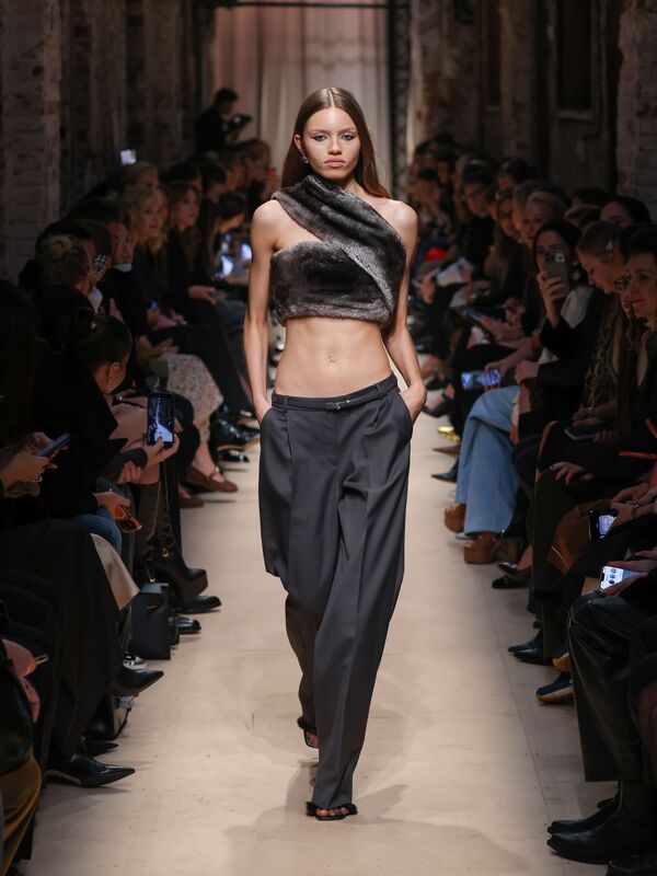Модель в асимметричном меховом топе и широких брюках серого цвета, создающих контраст с её стройной фигурой, на показе Sashaverse осень-зима 2026.