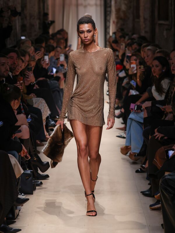 Модель в золотистом сетчатом мини-платье с длинными рукавами, дополняет образ меховым клатчем на показе Sashaverse осень/зима 2026.