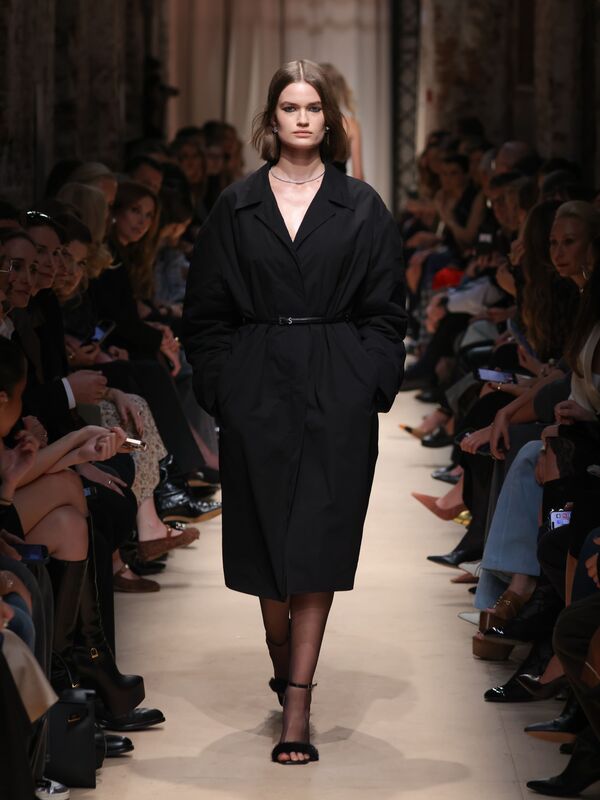 Модель в объемном черном пальто с поясом, сочетая элегантность и минимализм, уверенно шагает по подиуму осени-зимы 2026 от Sashaverse