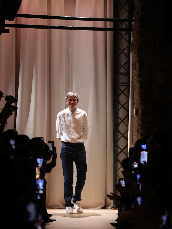 Дизайнер Sashaverse на финальном выходе, одетый в белую рубашку и темные джинсы, создает атмосферу непринужденной элегантности.