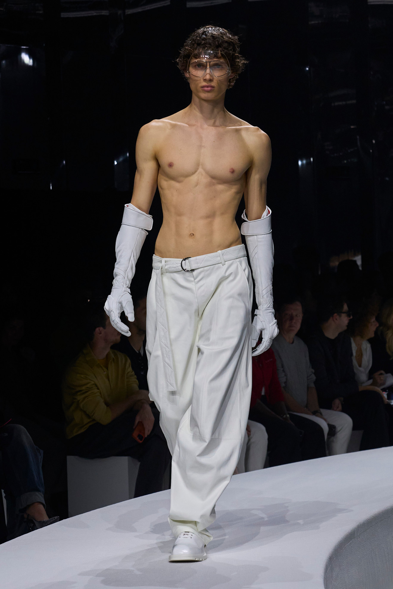 Модель в белых широких брюках и перчатках, демонстрирующая спортивную фигуру, создает атмосферу элегантной дерзости для весны/лета 2024 от Ferrari...