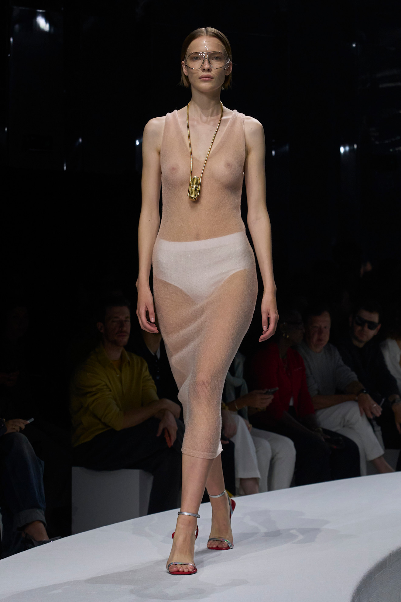 Прозрачное платье телесного цвета с легким блеском, дополненное массивным золотым ожерельем и стильными очками, создает эффектный образ для весны/лета 2024 от Ferrari....