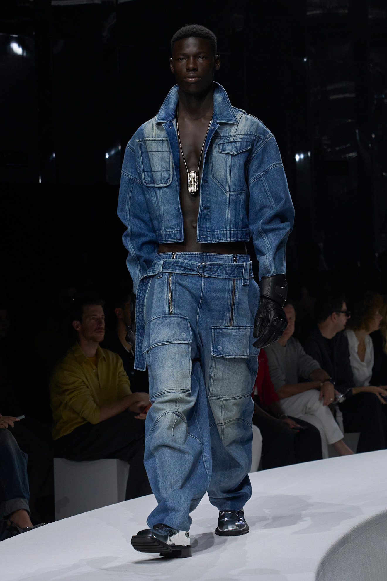 Модель в объемном джинсовом комплекте с открытой грудью и кожаными перчатками, подчеркивающими стильный образ для весны/лета 2024 от Ferrari