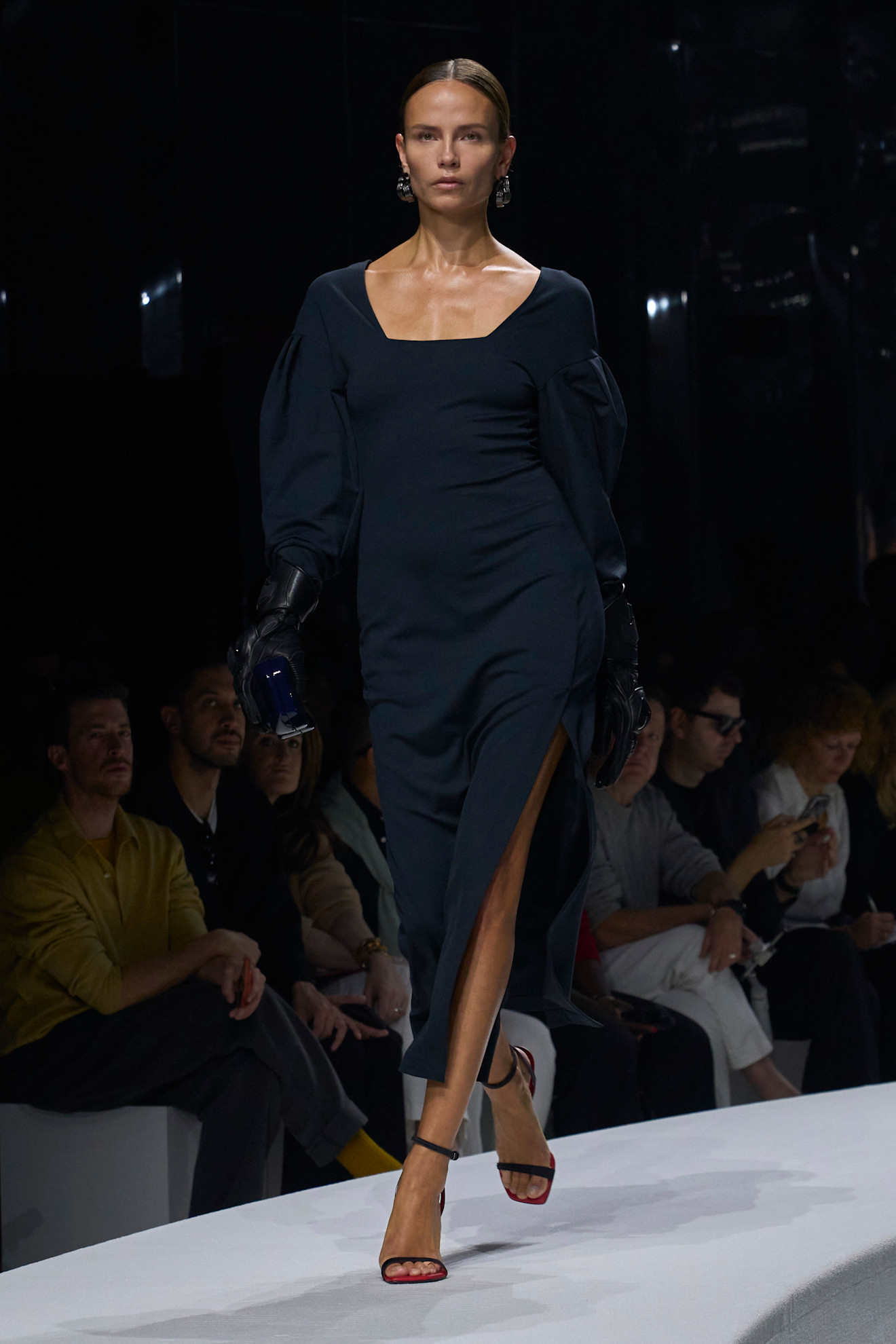 Элегантное темно-синее платье с объемными рукавами и разрезом, дополненное черными перчатками и красными босоножками, создает стильный образ....