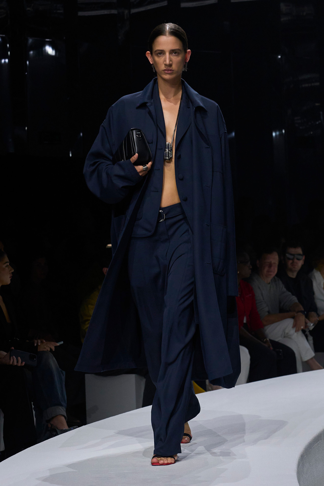 Модель в свободном темно-синем костюме с открытым животом и длинным пальто, дополненная стильной сумкой и минималистичными украшениями