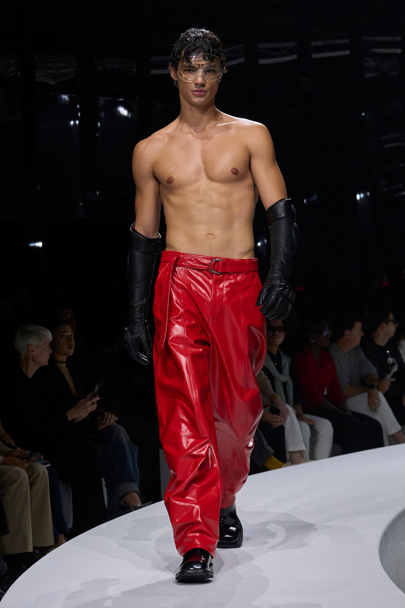 Модель в ярких красных кожаных штанах и черных перчатках демонстрирует смелый стиль на показе Ferrari весна/лето 2024.