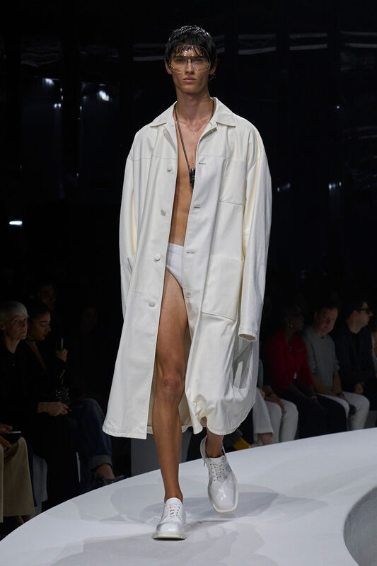 Модель в объемном белом тренче и минималистичных кроссовках, создающих легкий и современный образ для весны/лета 2024 от Ferrari