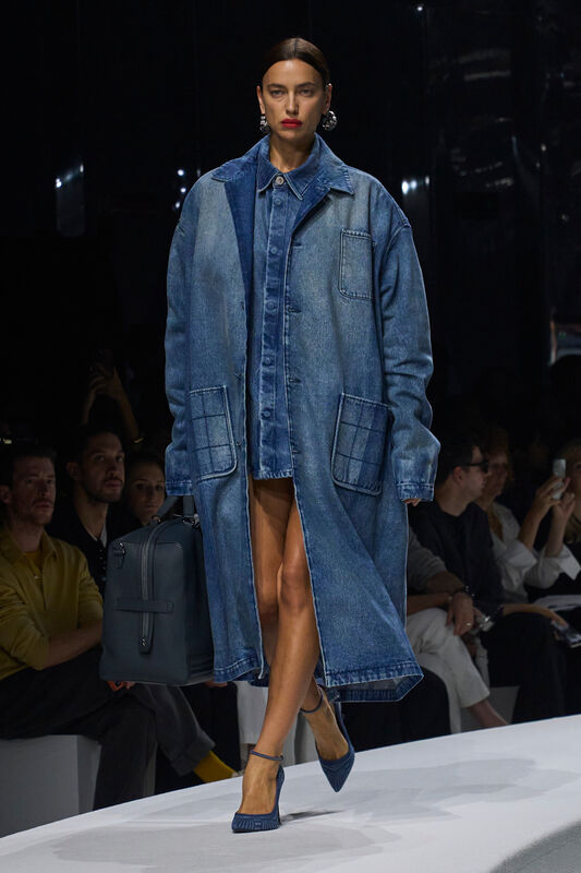 Модель в объемном джинсовом пальто с карманами, сочетает с коротким платьем и стильной сумкой, создавая эффектный образ для весны-лето 2024 от Ferrari...