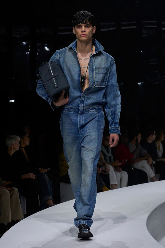 Мужской комбинезон из светлого денима с открытой грудью, дополненный стильной сумкой, создает атмосферу уверенности и современности.