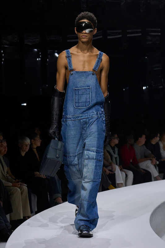 Модель в комбинезоне из денима с асимметричными деталями, дополненном кожаными перчатками и стильными очками, создает атмосферу современного уличного шика....