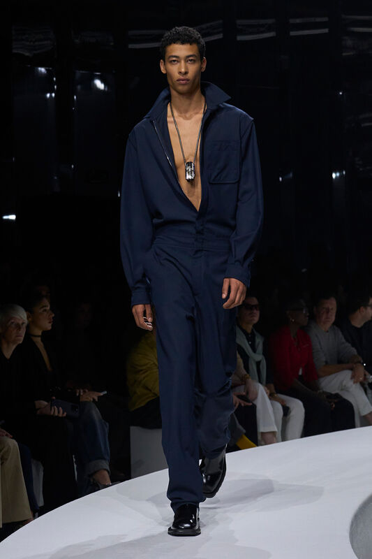 Мужской комбинезон глубокого синего цвета с открытым воротником, дополненный стильным аксессуаром, создает атмосферу уверенности и современности....