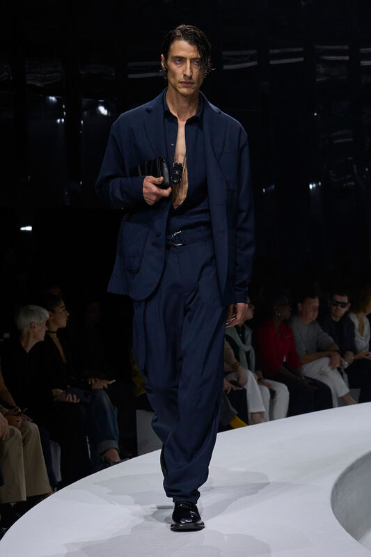 Мужская коллекция Ferrari весна/лето 2024: строгий темно-синий костюм с открытой рубашкой и акцентом на аксессуары, создающий эффектный образ.