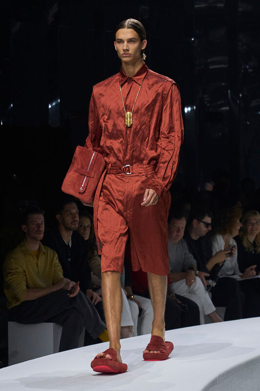 Мужская коллекция Ferrari весна/лето 2024: блестящая рубашка и шорты терракотового оттенка, дополненные стильной сумкой и сандалиями.