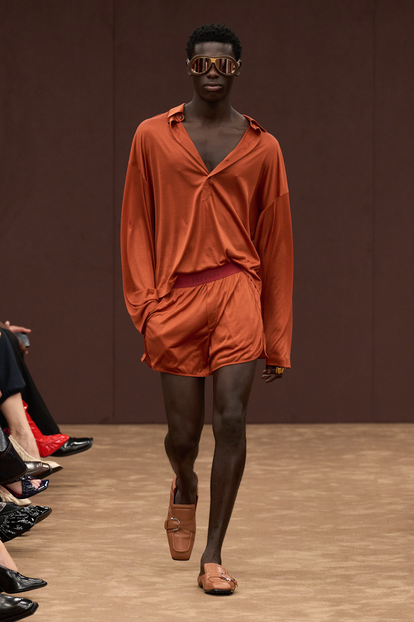 Модель в свободной оранжевой рубашке и шортах, дополненная стильными солнцезащитными очками и обувью с пряжкой, создает атмосферу летнего шика....