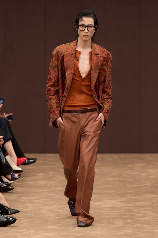 Мужской образ от Ferrari: жакет с абстрактным узором в теплых тонах, облегающий топ и широкие брюки, создающие стильный контраст.