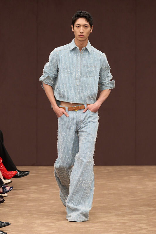 Модель в светло-голубом комплекте из фактурной ткани с рифленой поверхностью, свободные брюки и укороченная рубашка, стильный акцент на поясе....