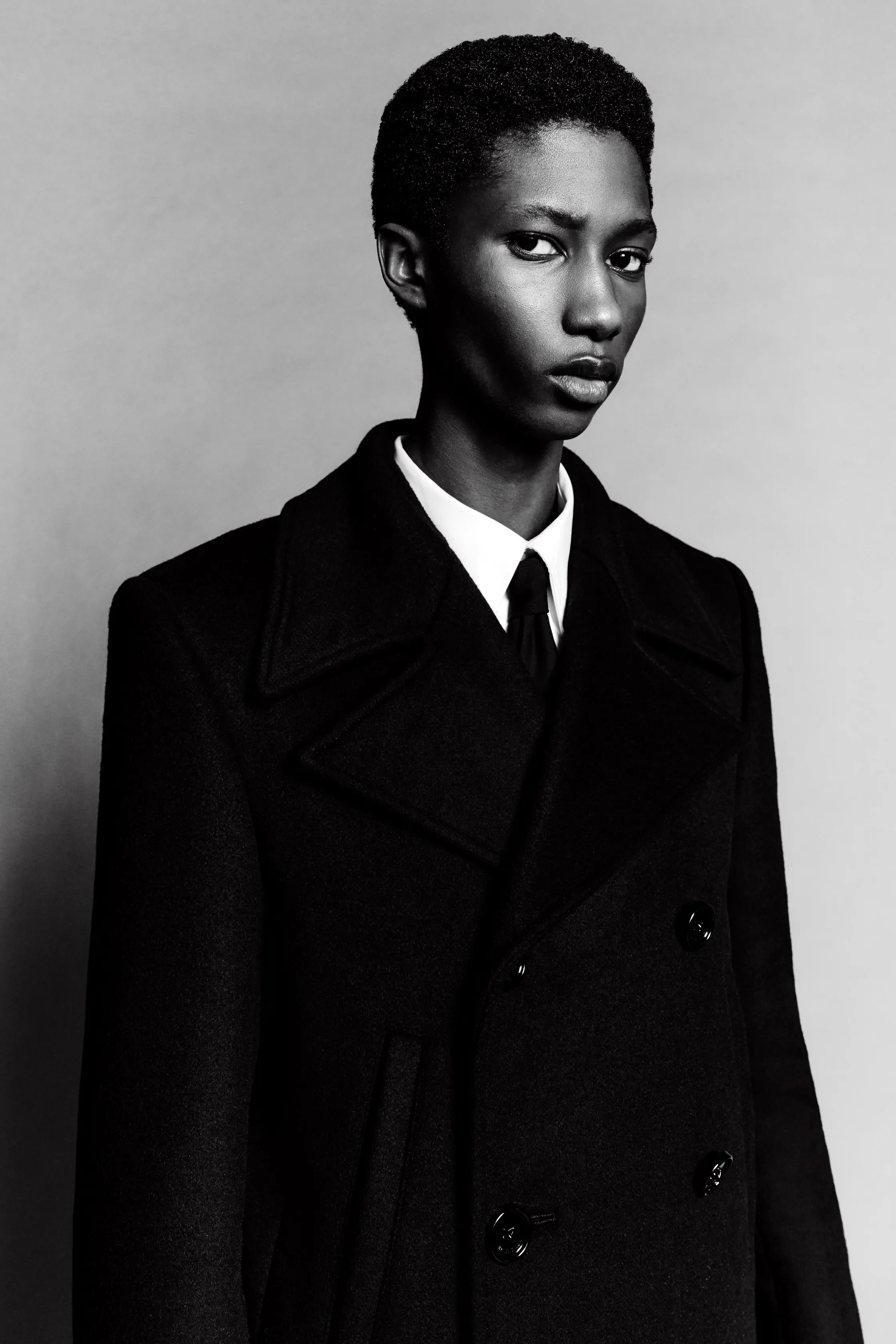 Портрет в черном пальто с классическим воротником и строгой белой рубашкой, передающий атмосферу уверенности и элегантности