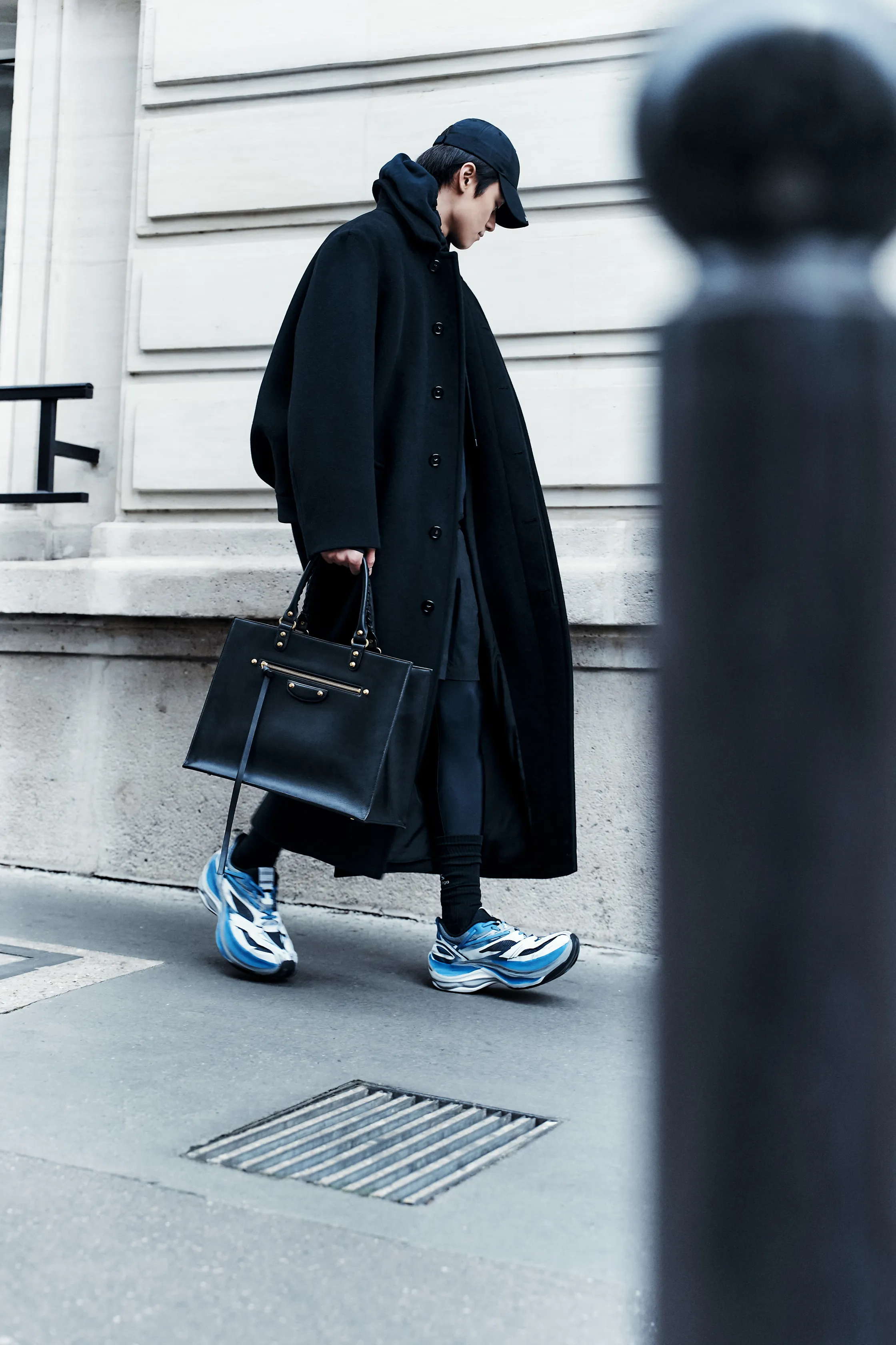 Модель в длинном черном пальто и спортивной одежде, с акцентом на стильные кроссовки, создает образ городской элегантности