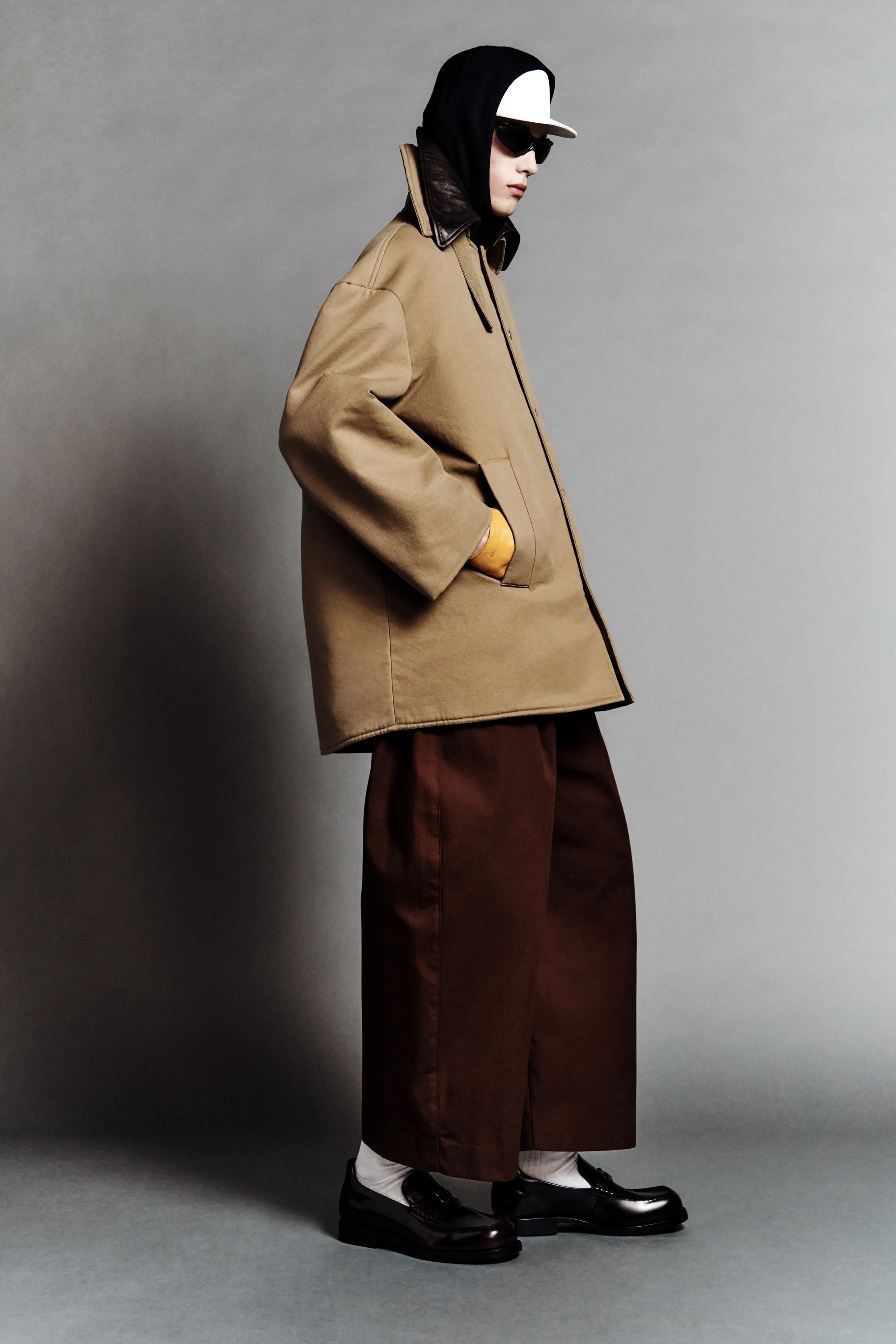 Строгий силуэт: модель в объемном бежевом пальто и широких брюках, завершает образ кепка и солнцезащитные очки