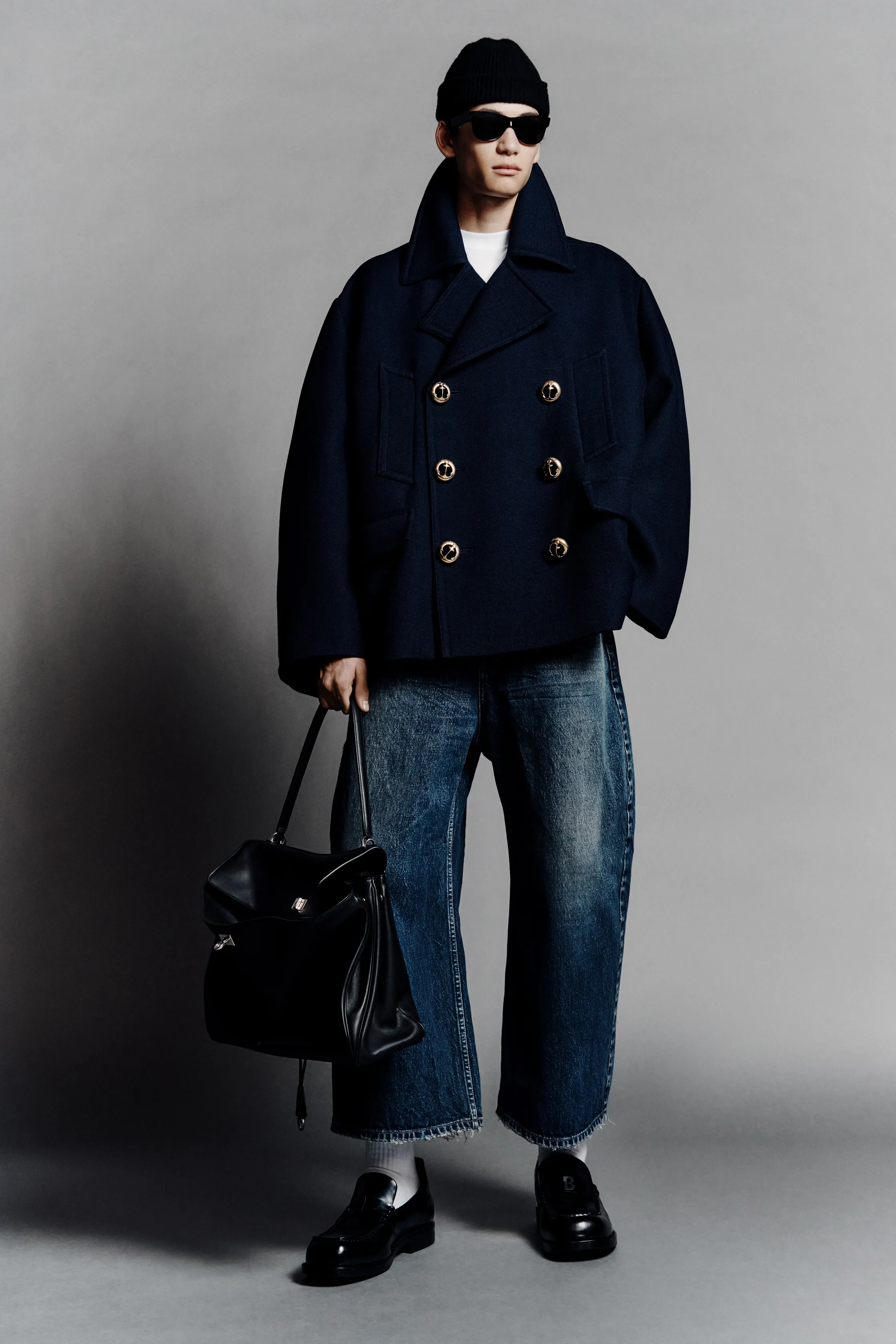 В темно-синем пальто с золотыми пуговицами, модель держит черную сумку, сочетая элегантность и повседневность