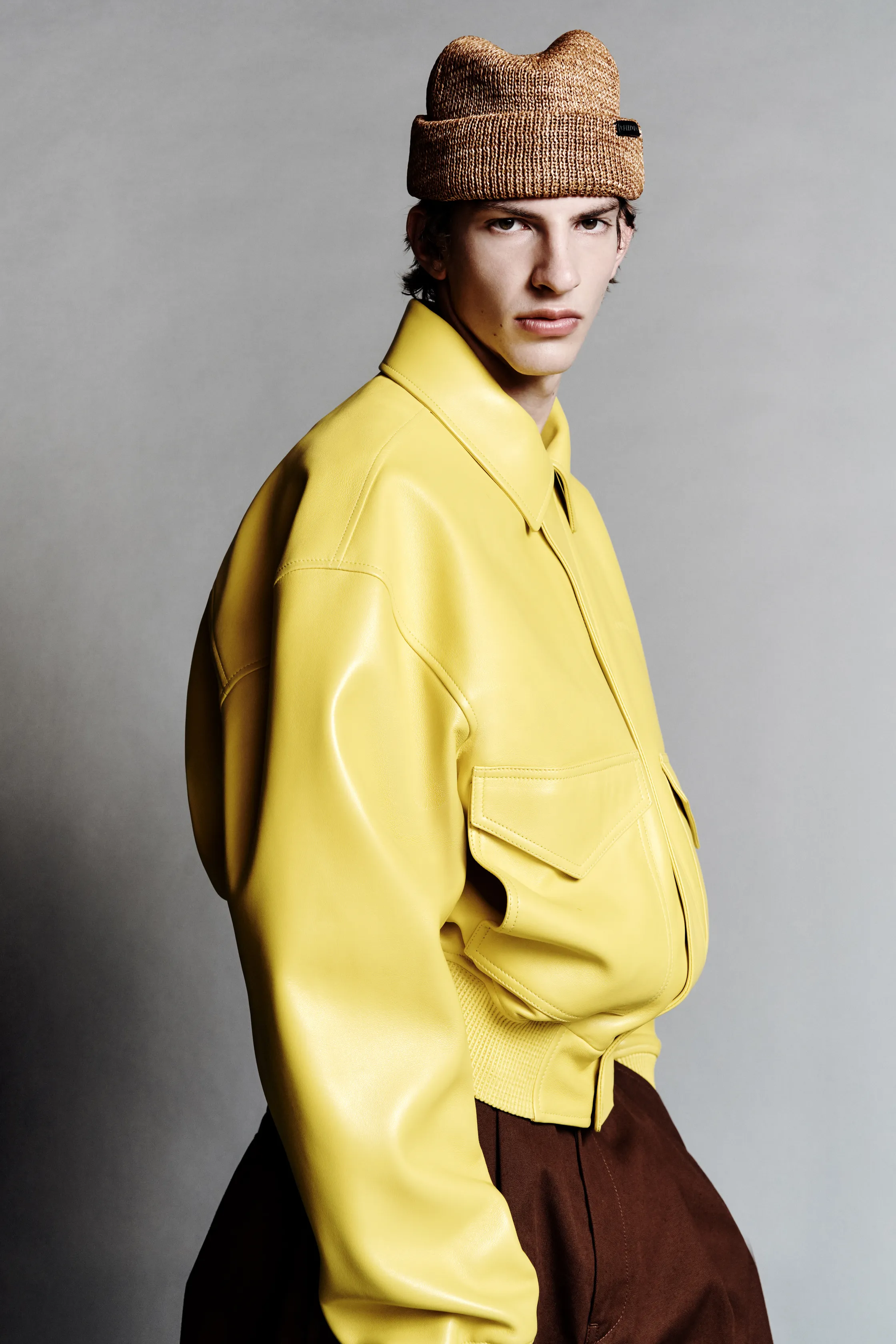 Яркая кожаная куртка желтого цвета в сочетании с коричневыми брюками, модель смотрит в камеру с уверенным выражением