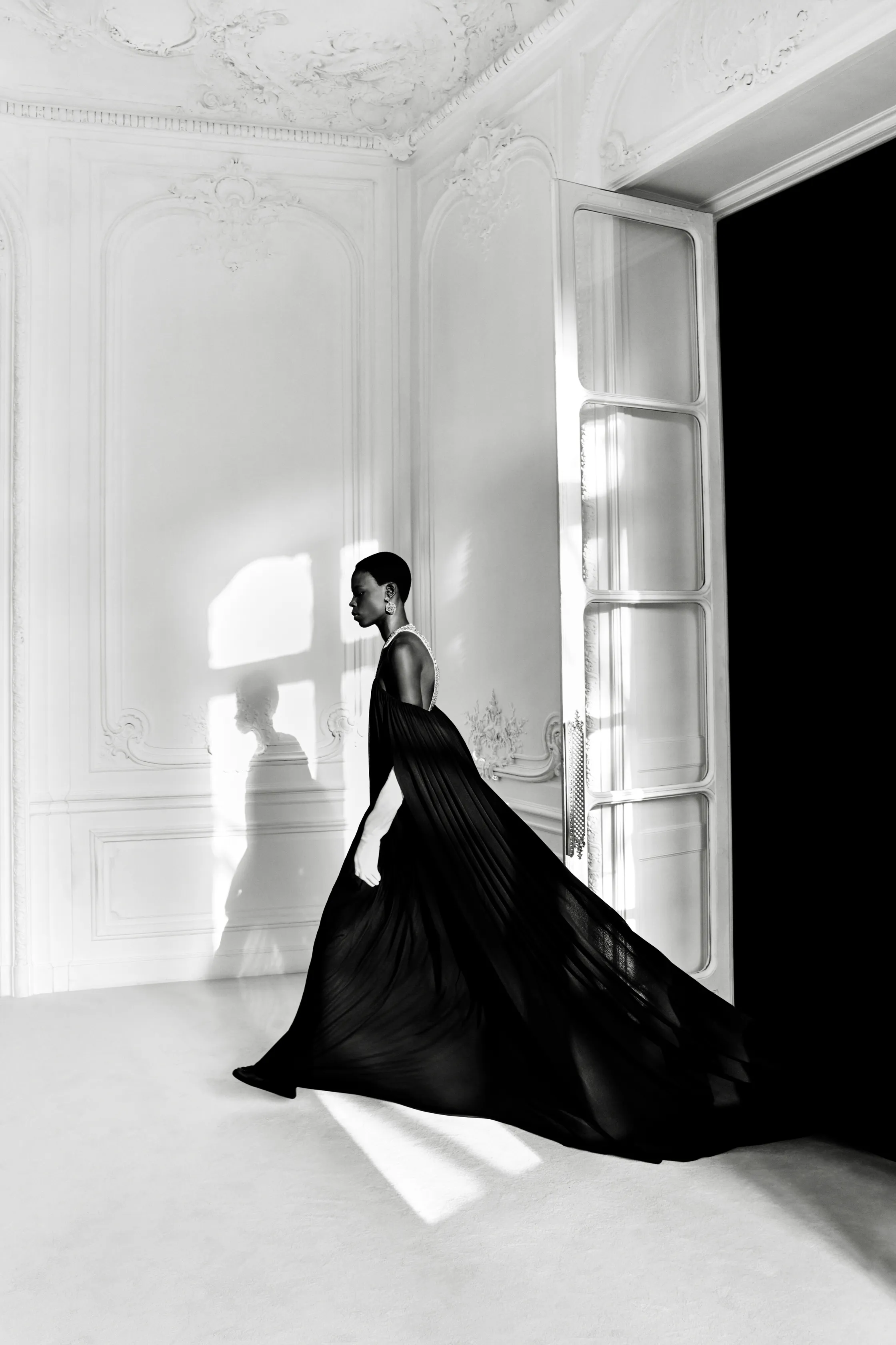 Платье из черного шифона с длинным шлейфом, модель грациозно движется по светлому помещению, создавая атмосферу загадки