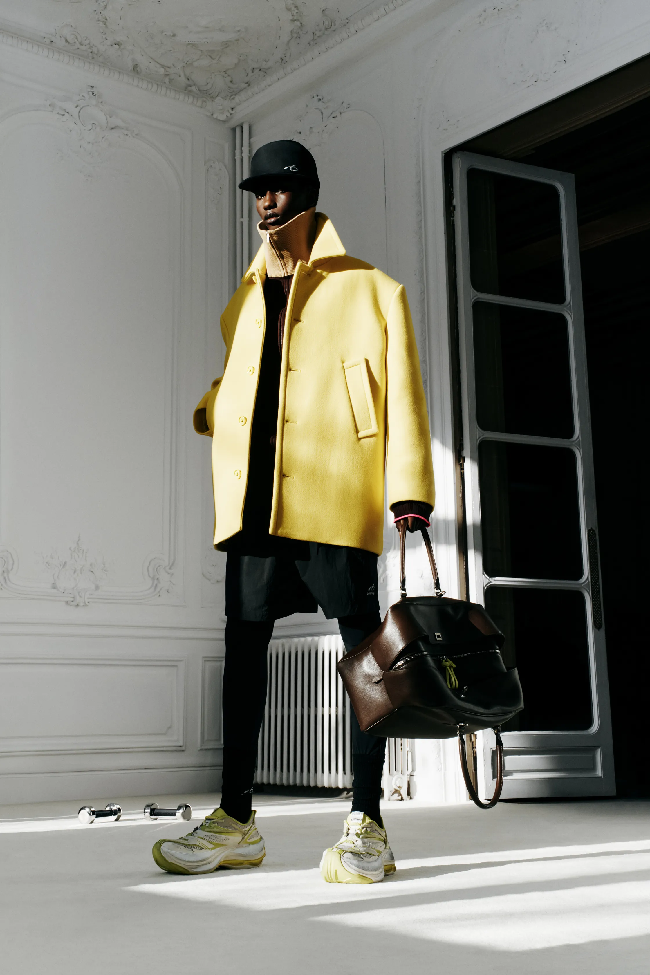Яркий желтый пальто с крупными пуговицами, черные леггинсы и кроссовки, создающие спортивный контраст в интерьере.