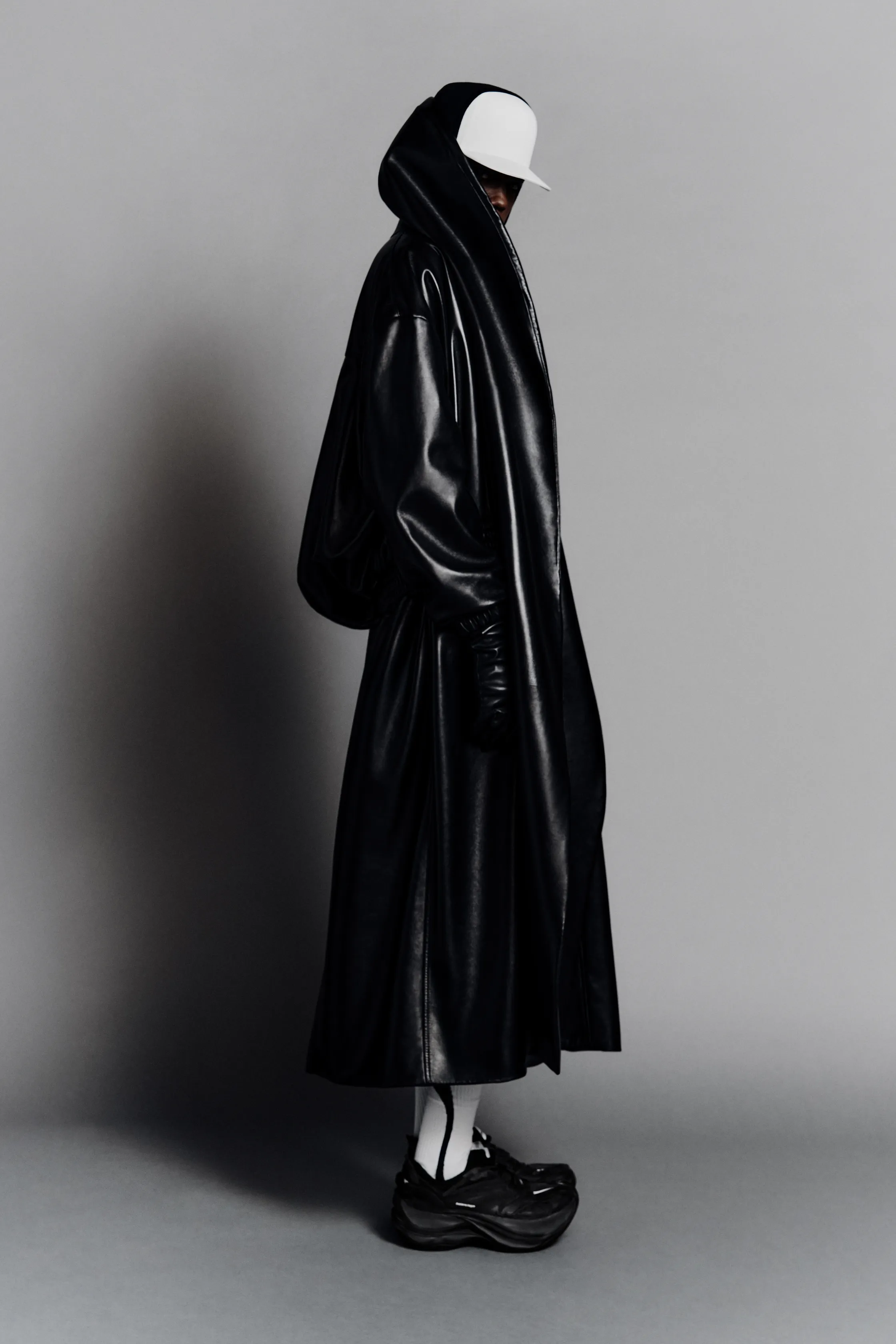 Объемный черный плащ с капюшоном, создающий загадочный силуэт на фоне серой стены