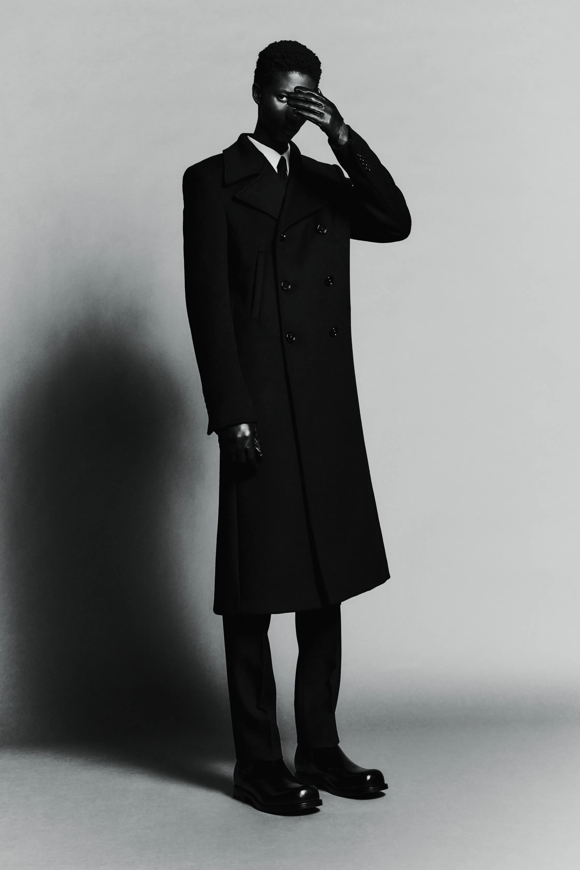 Строгий черный пальто с двойным рядом пуговиц, создающее эффектный контраст с серым фоном