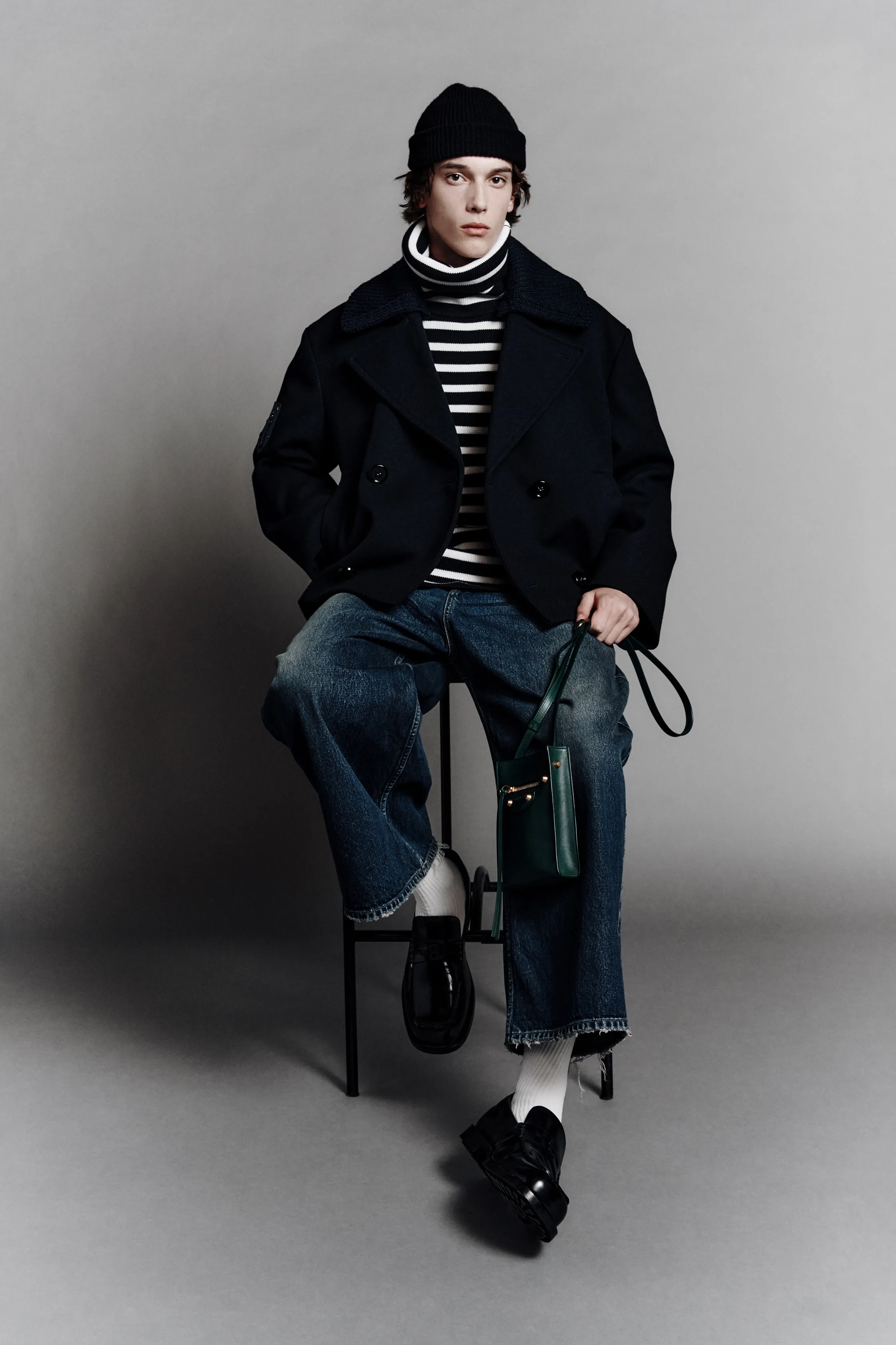 Стильный образ с черным двубортным пальто и полосатым свитером, дополненный широкими джинсами и зеленой сумкой