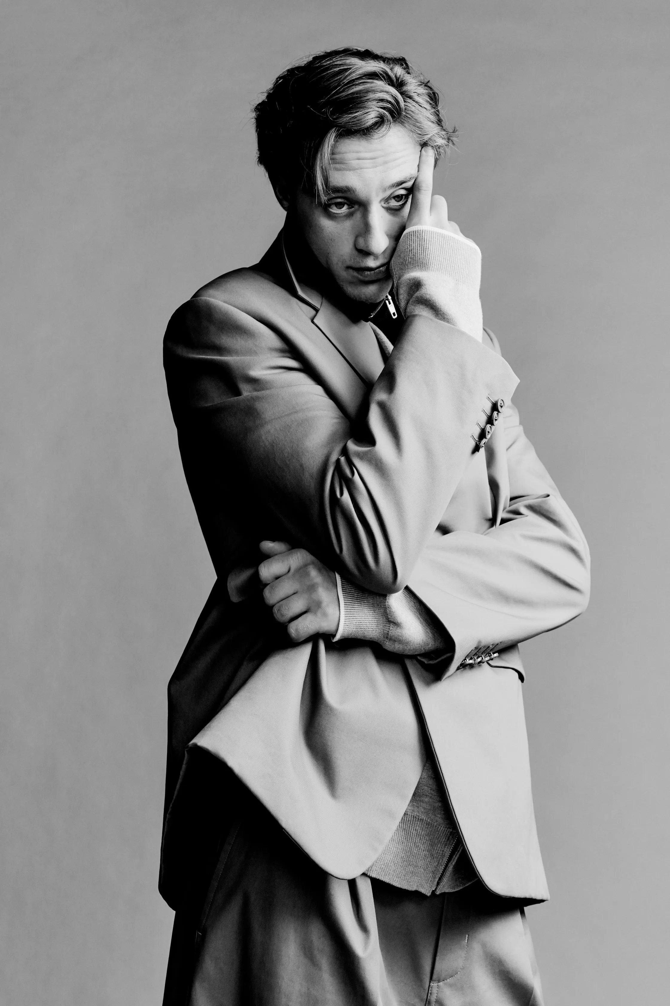 Модель в стильном сером костюме с выразительной позой, создающей атмосферу загадочности и уверенности