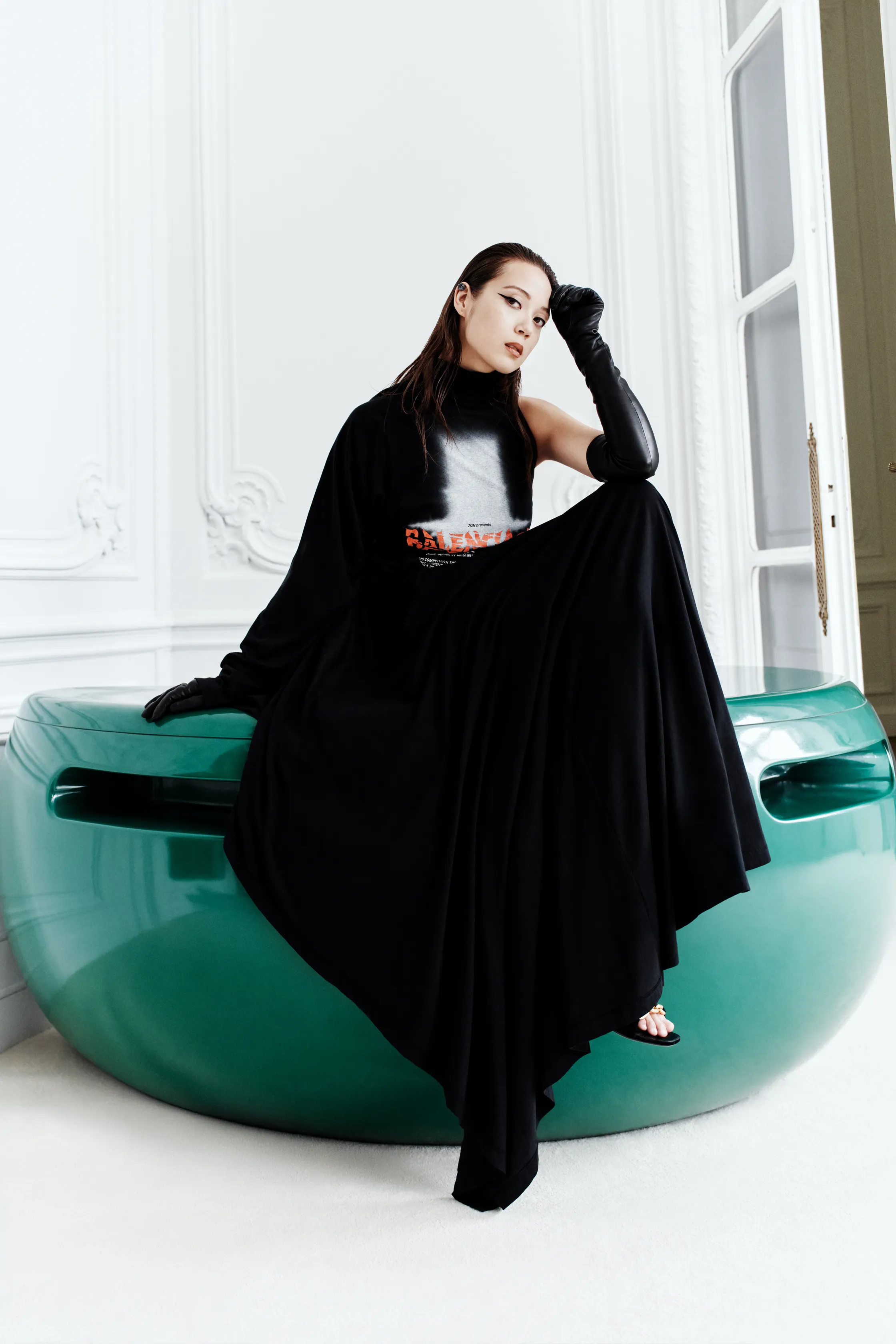 Элегантное черное платье с асимметричным кроем, акцент на перчатках и контрастном декоре, сидя на зеленом объекте