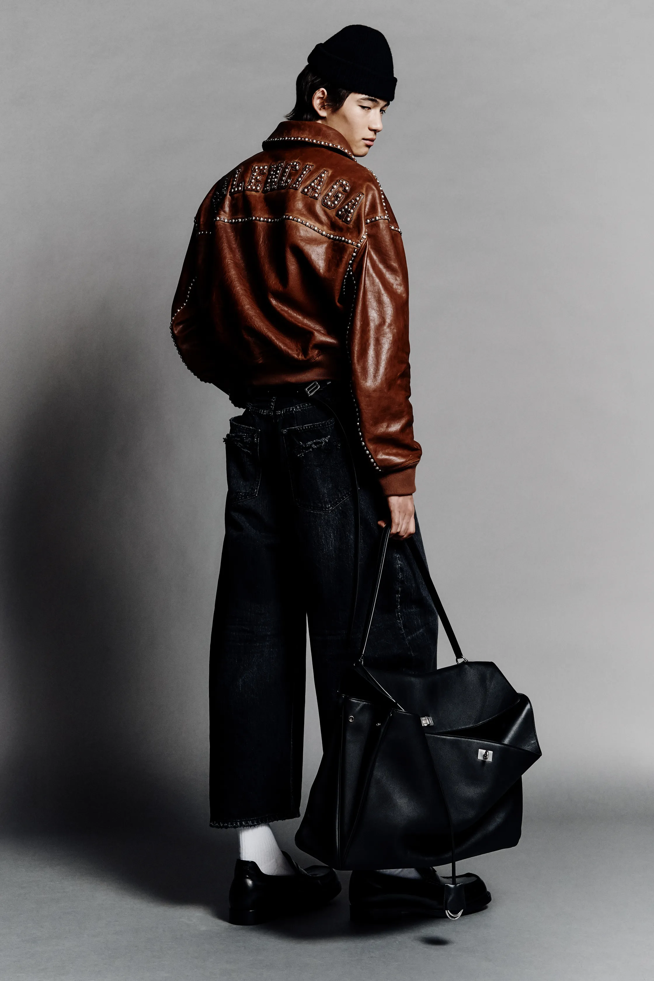 Кожаная куртка с заклепками и широкие джинсы, образ завершает черная сумка и стильная шапка, создавая дерзкий лук