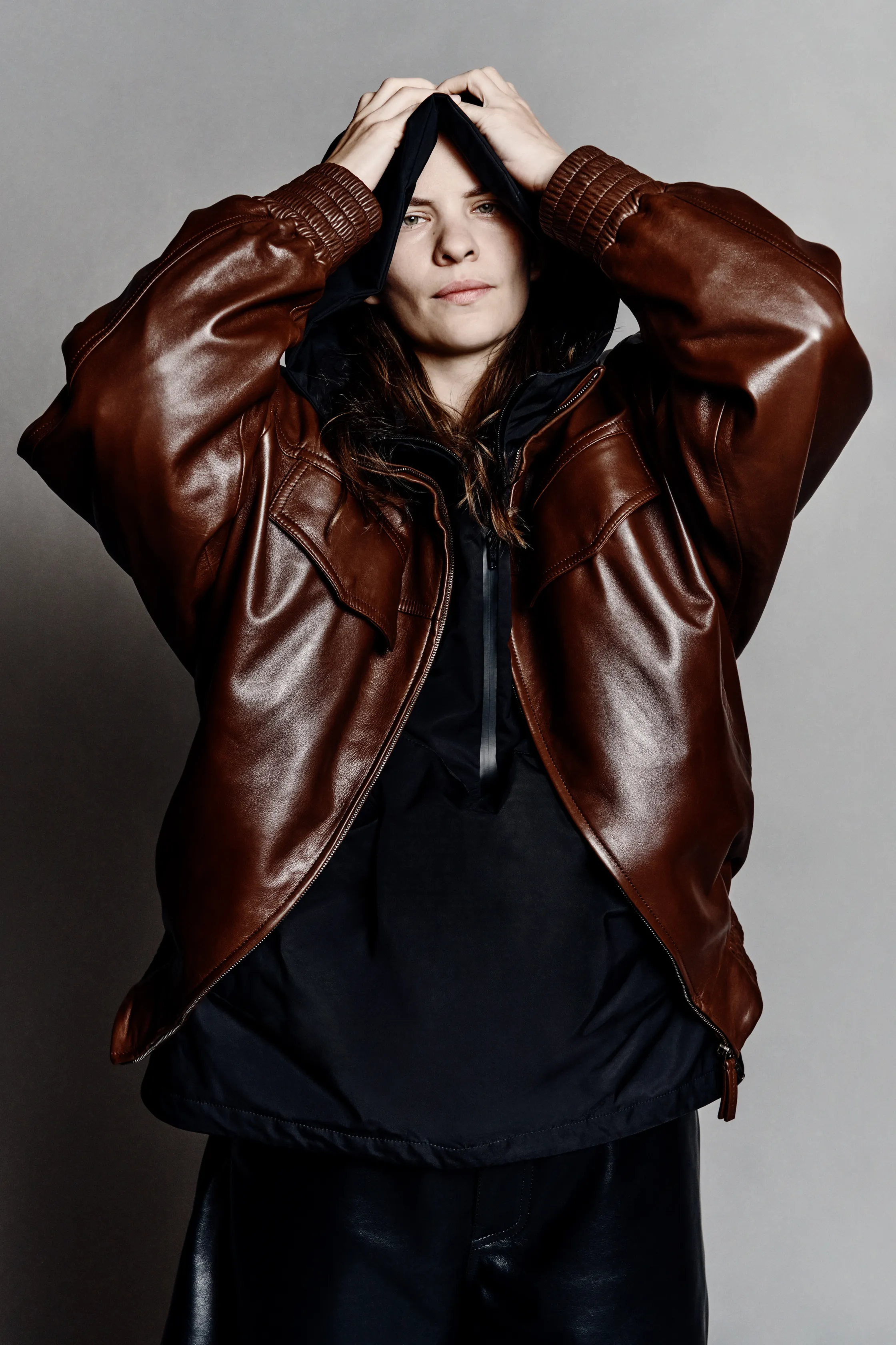 Широкая коричневая кожаная куртка с черным капюшоном, создающая эффектный и дерзкий образ для осени