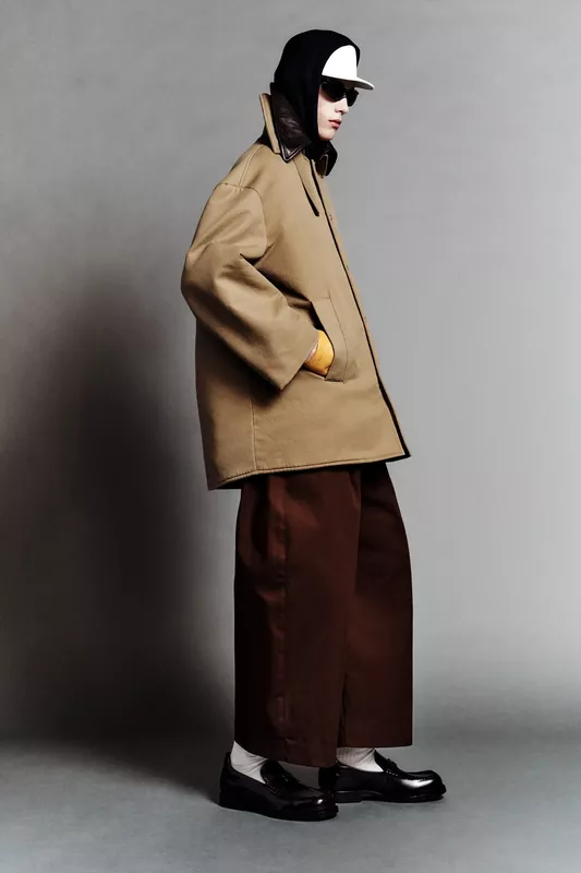 Строгий силуэт: модель в объемном бежевом пальто и широких брюках, завершает образ кепка и солнцезащитные очки