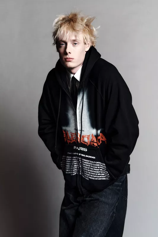 Модель в черном худи с ярким принтом и джинсах, с небрежной прической, создает атмосферу уличного стиля