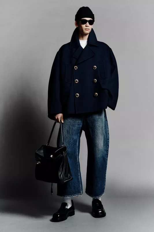 В темно-синем пальто с золотыми пуговицами, модель держит черную сумку, сочетая элегантность и повседневность