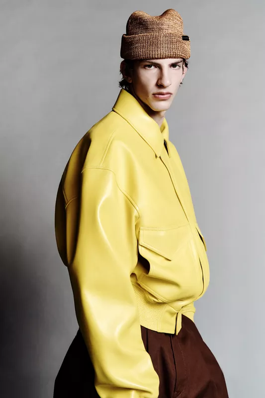 Яркая кожаная куртка желтого цвета в сочетании с коричневыми брюками, модель смотрит в камеру с уверенным выражением